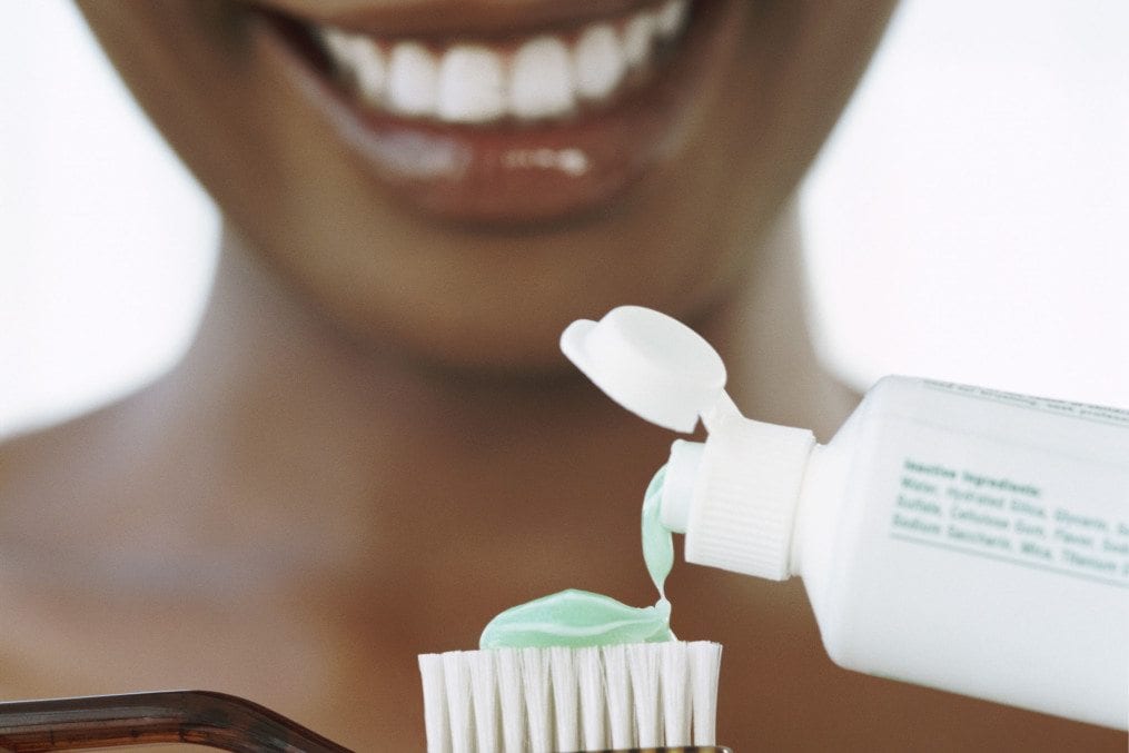 Close-up of a Smiling Young Woman Squeezing Toothpatse onto a Toothbrush